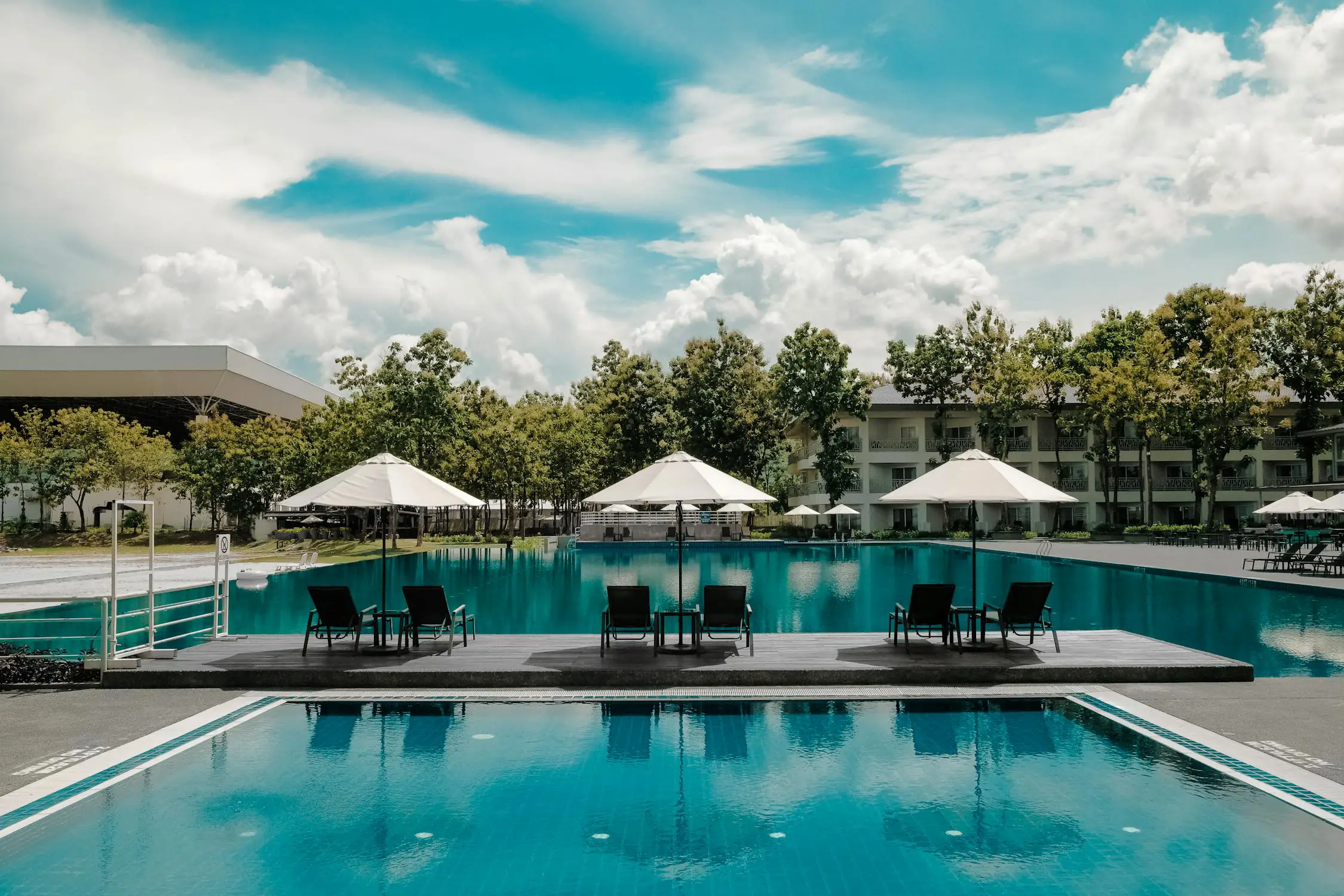 Black lounge chairs near a pool under white cloudy blue skies