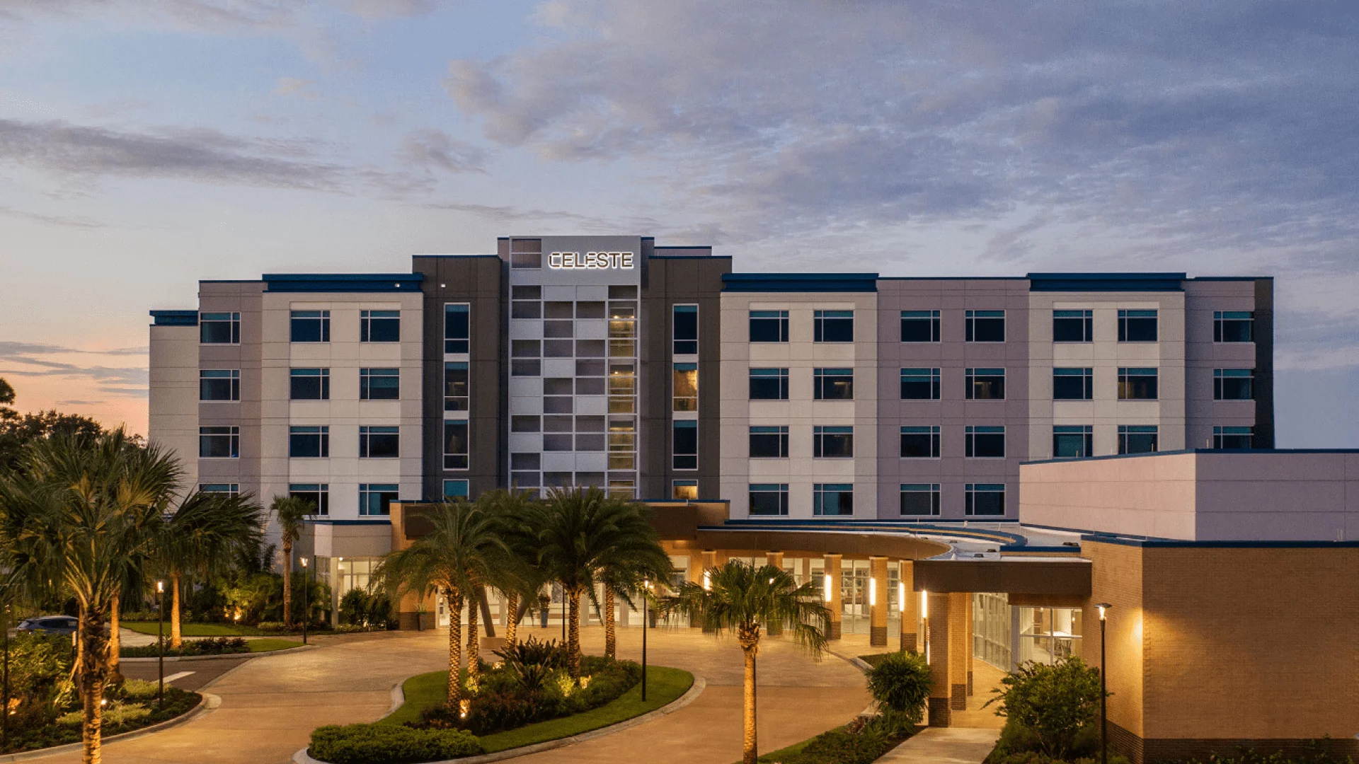 Modern hotel building named Celeste with palm trees and a circular driveway at sunset, under a partly cloudy sky.