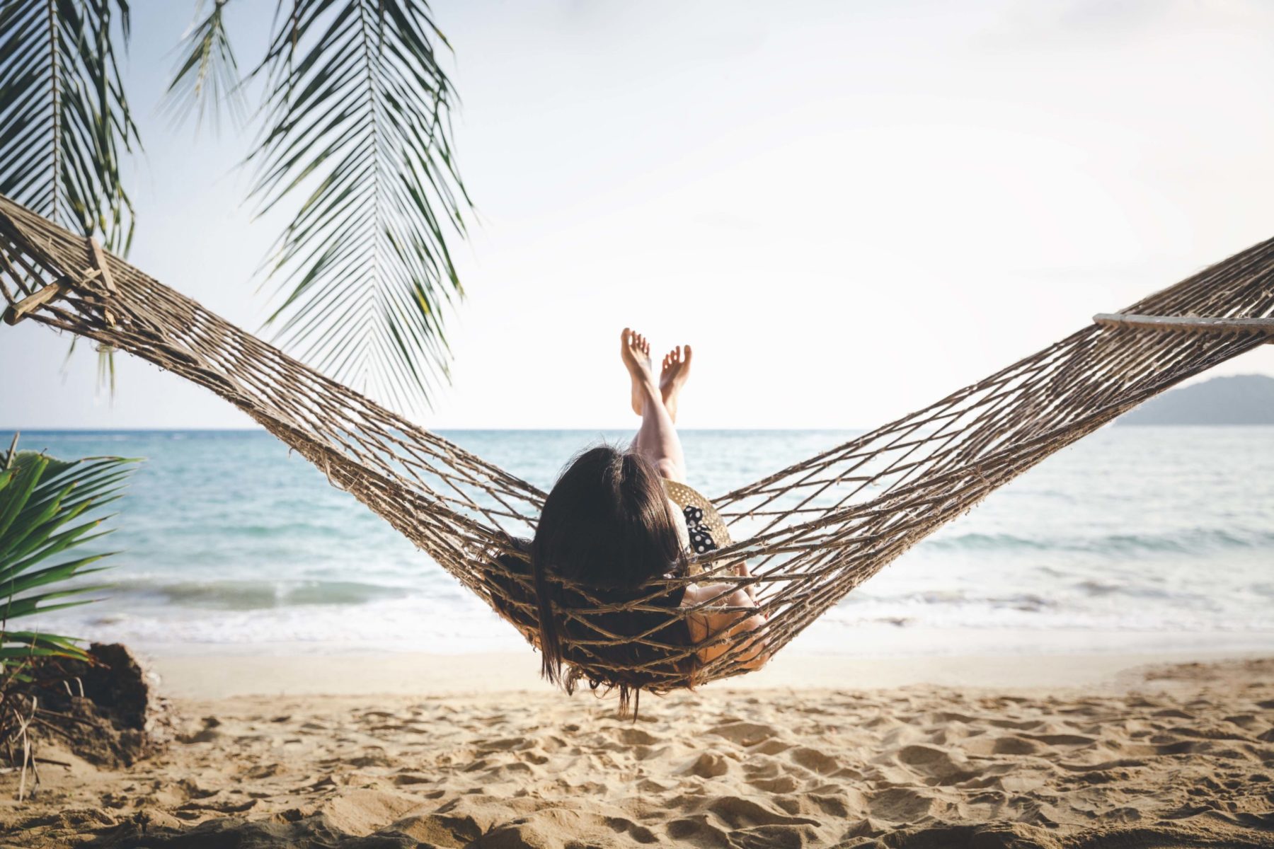 woman with white bikini, hat and shorts Jeans relaxing in hammock on tropical beach at sunset