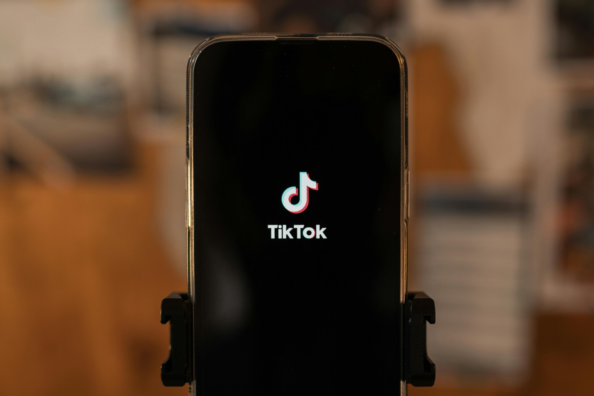 A smartphone displays the TikTok logo and name on its screen, with a blurred background behind it.
